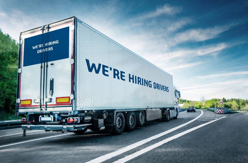 A truck with line "we're hiring drivers" driving on the highway.
