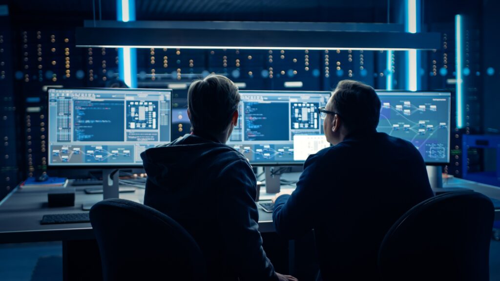 Two workers looking at their computers and discussing the virtual twins of factories.