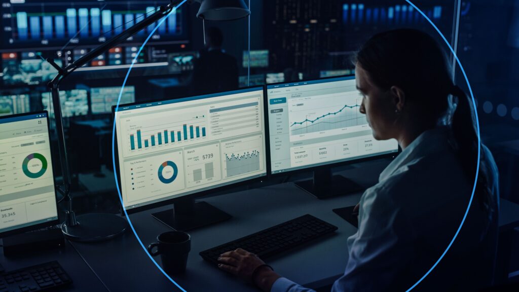 A worker sits in front of several computer screens showing data and graphs - AI and business - Dassault Systemes