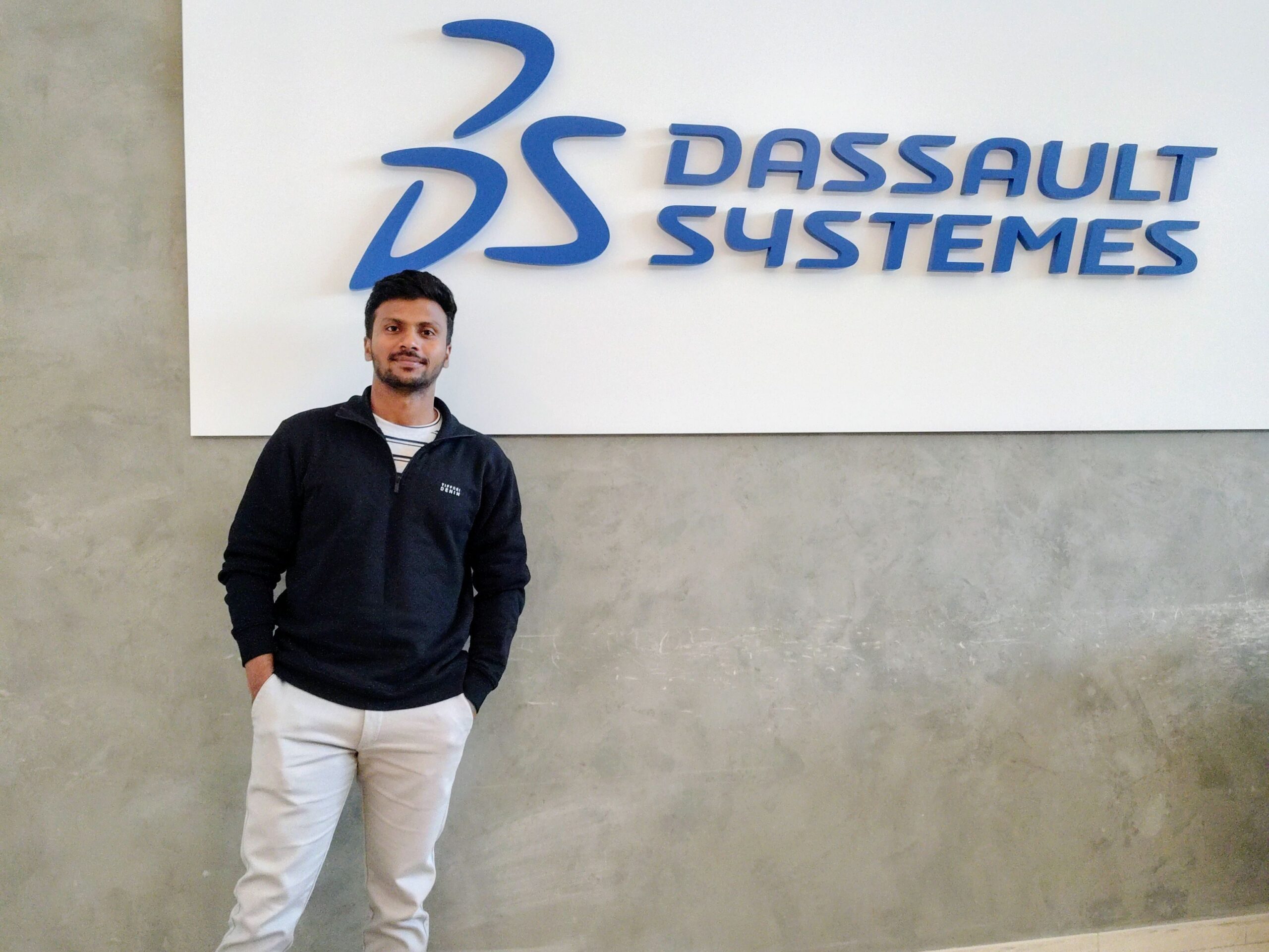 Nishanth Nagesh, Data Science Intern for ENOVIA, poses in front of the Dassault Systèmes sign.